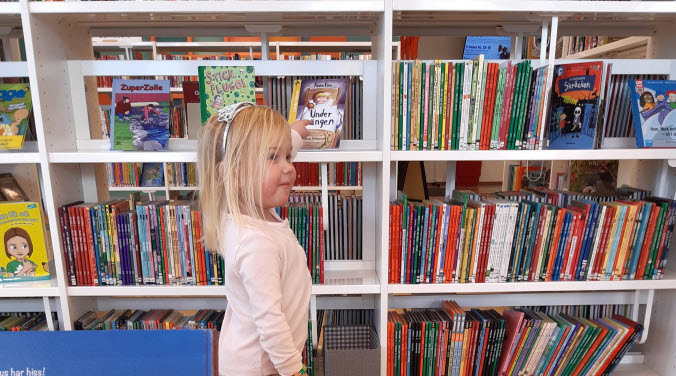 Barn står och väljer böcker på bibliotek